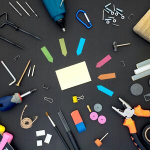 A black table with a host of office supplies on it including post-its pensicls, erasers, tacks and more.