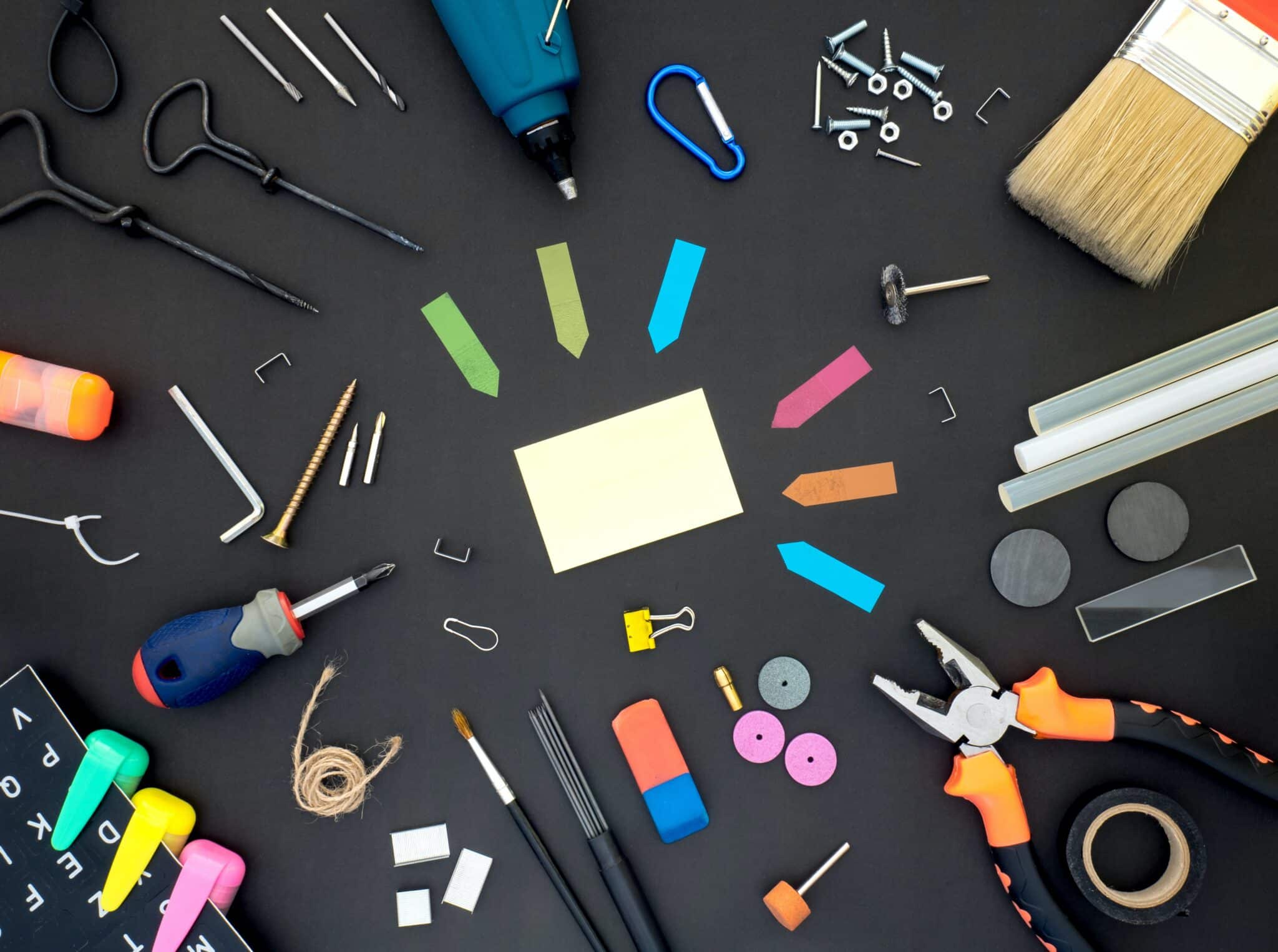 A black table with a host of office supplies on it including post-its pensicls, erasers, tacks and more.