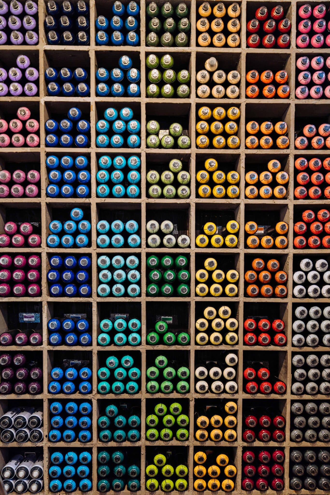 Different color spray paints organized in cubbies according to their color.
