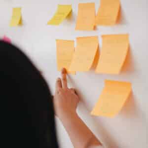 Post-it notes on a white board, with a woman standing in front of them pointing at one.