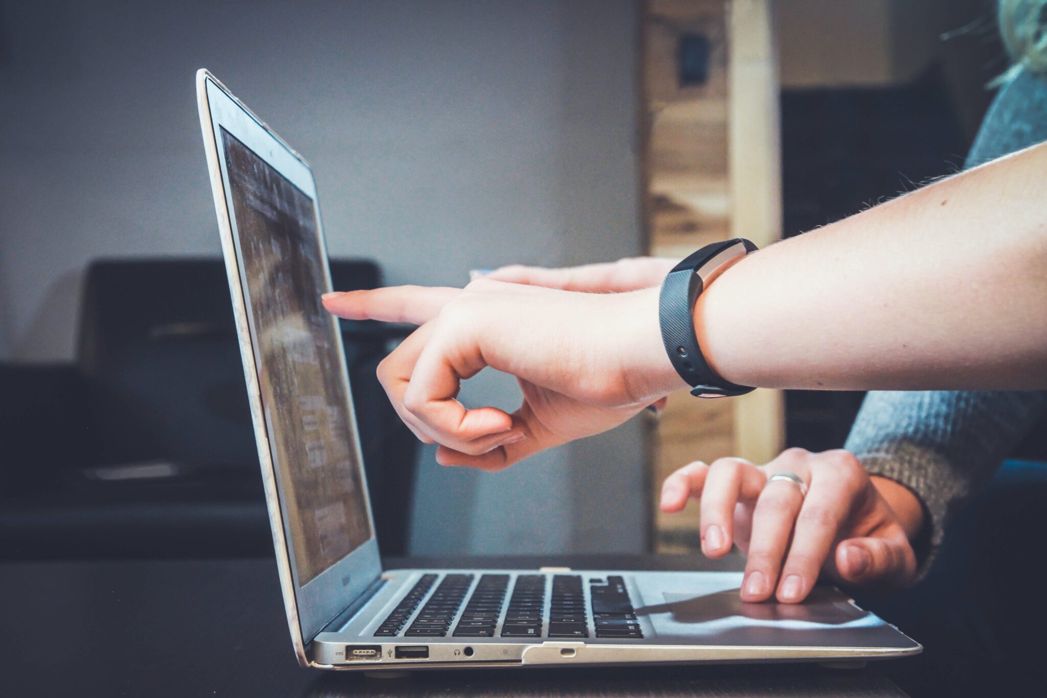 Two sets of hands pointing at a laoptop screen.