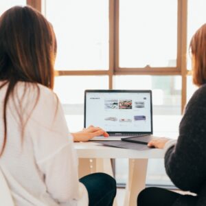 Two women in an office looking at a laptop screen with analytics on it.