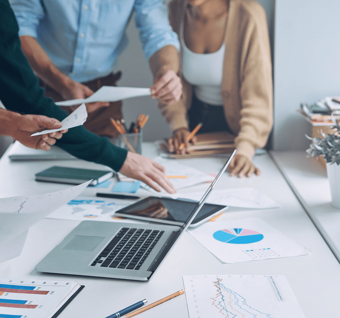 Group of people hands reviewing papers around a white table.