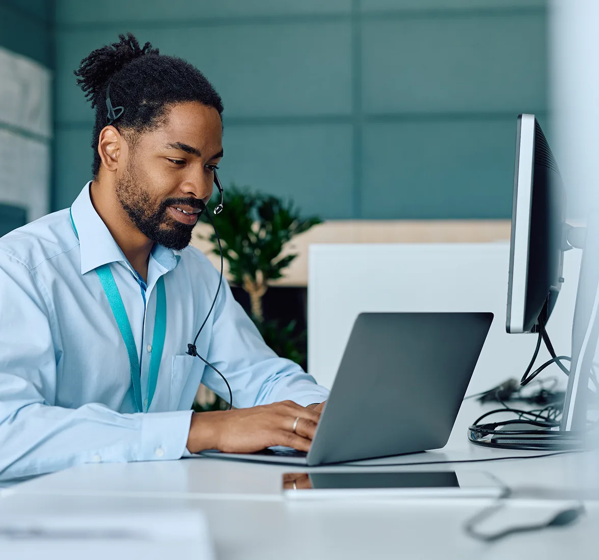 Picture of a man wearing a blue collar shirt working on a laptop in a office space